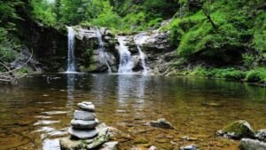 Peaceful forest waterfall with serene stone cairn, ideal for nature and travel themes.